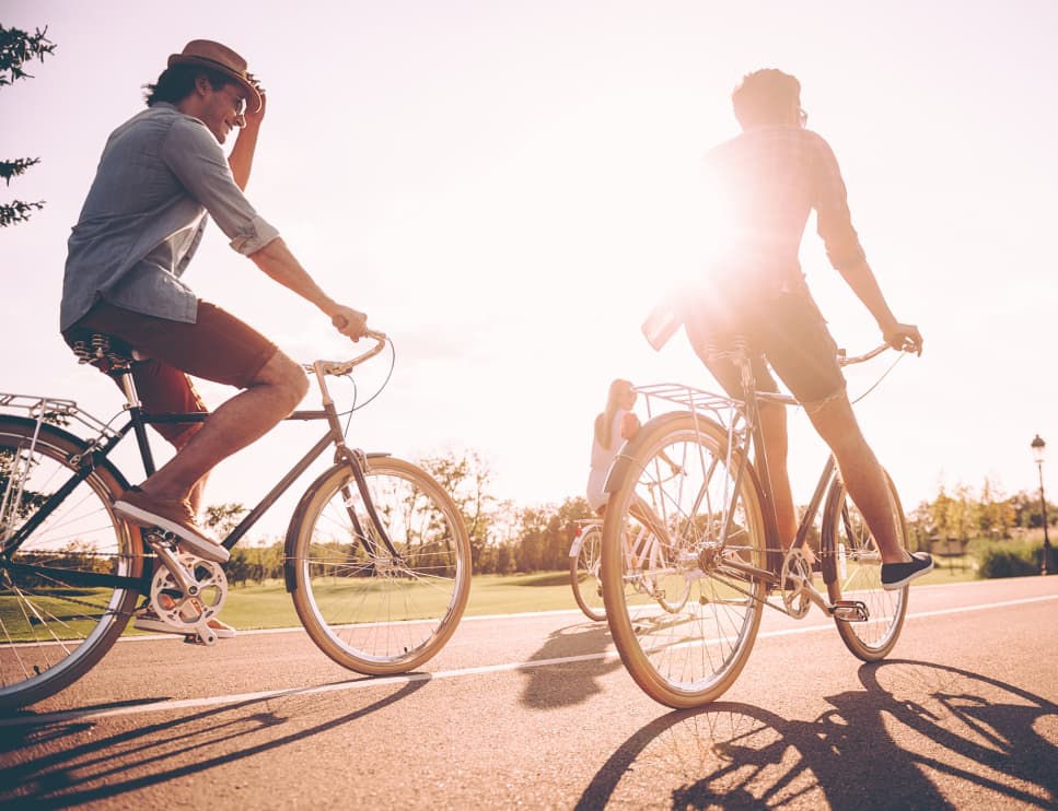 Two people ride bikes with the sun out