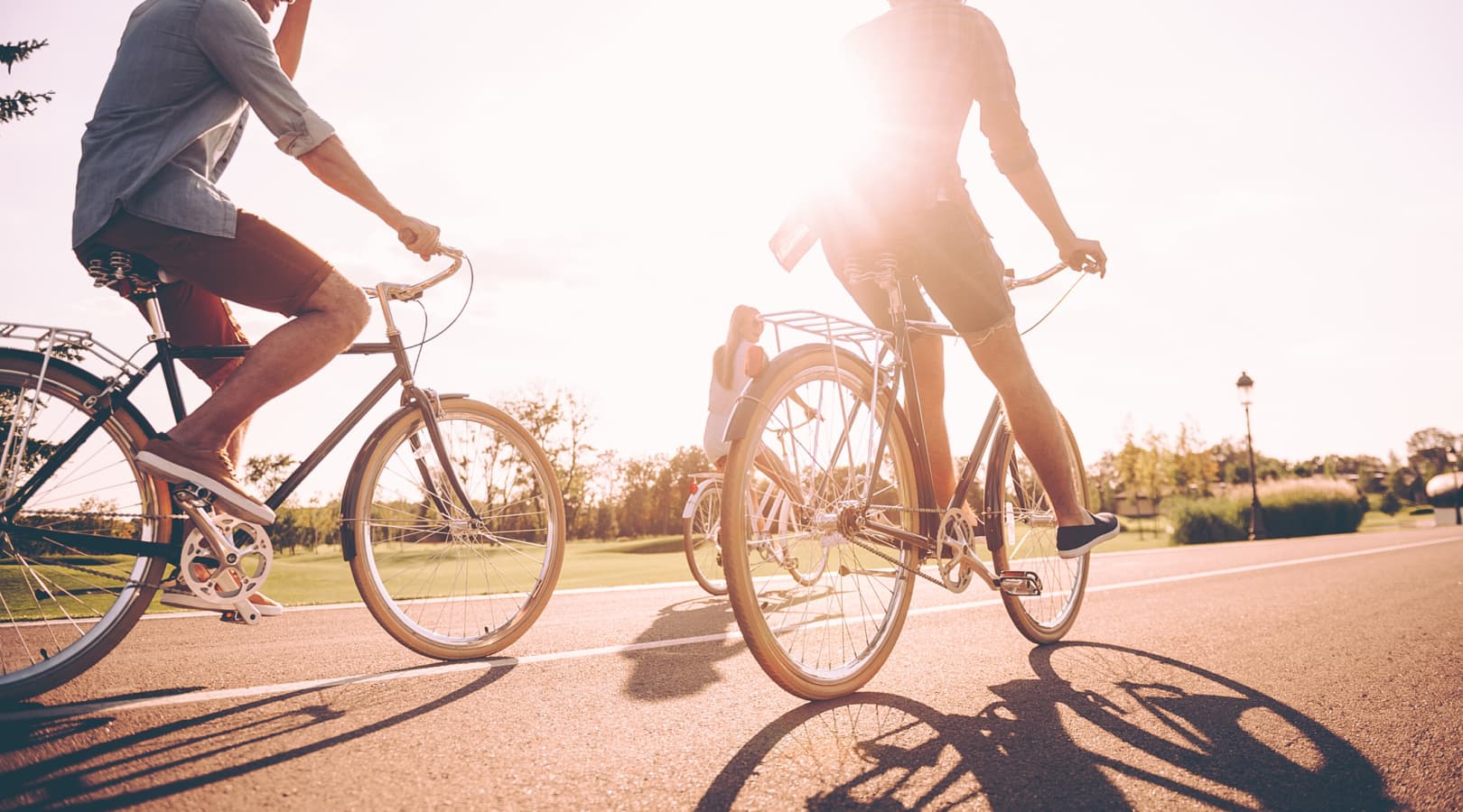 Two people ride bikes with the sun out