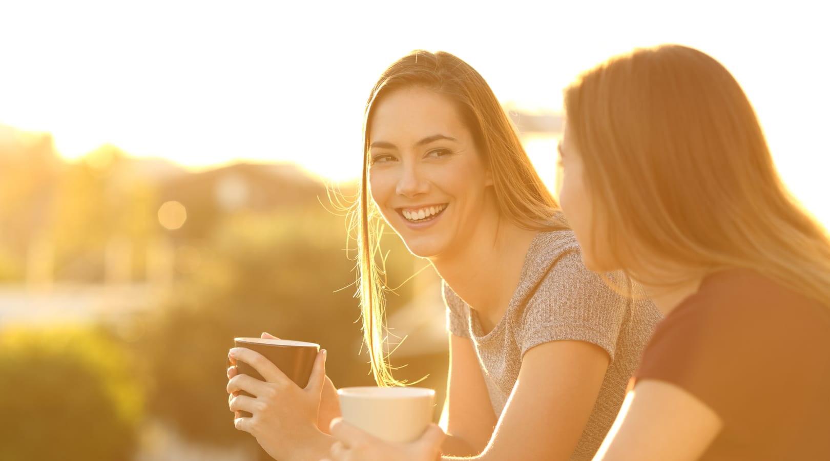 Two women smiling with coffee mugs in their hands