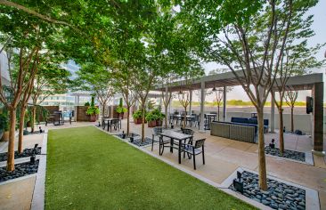 Side view of poolside gated courtyard, surrounded by trees and planters with picnic tables at MAA Lenox luxury apartment homes in Atlanta, GA