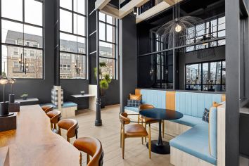 Modern coworking lounge area with multiple sitting areas on wood floors with dark walls and large picture windows at MAA Plaza Midwood luxury apartments in Charlotte, NC