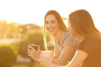 Two women smiling with coffee mugs in their hands 