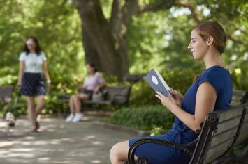 Woman reading book outside with others in the background 