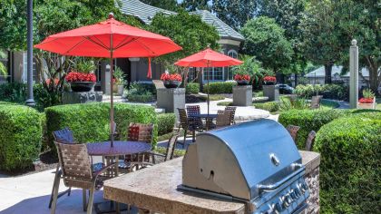 Patio tables and chairs with sun umbrellas and outdoor grilling station at MAA Heathrow luxury apartments in Orlando, FL