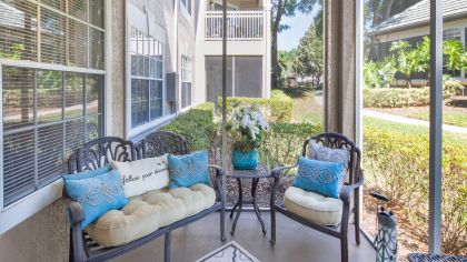 Spacious screened-in patio with cushioned loveseat and chairs with a garden view at MAA Heathrow luxury apartments in Orlando, FL