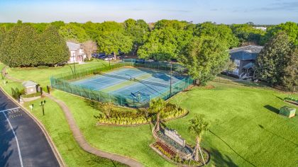 Aerial view of lighted tennis courts surrounded by lush green landscape at MAA Heathrow luxury apartments in Orlando, FL