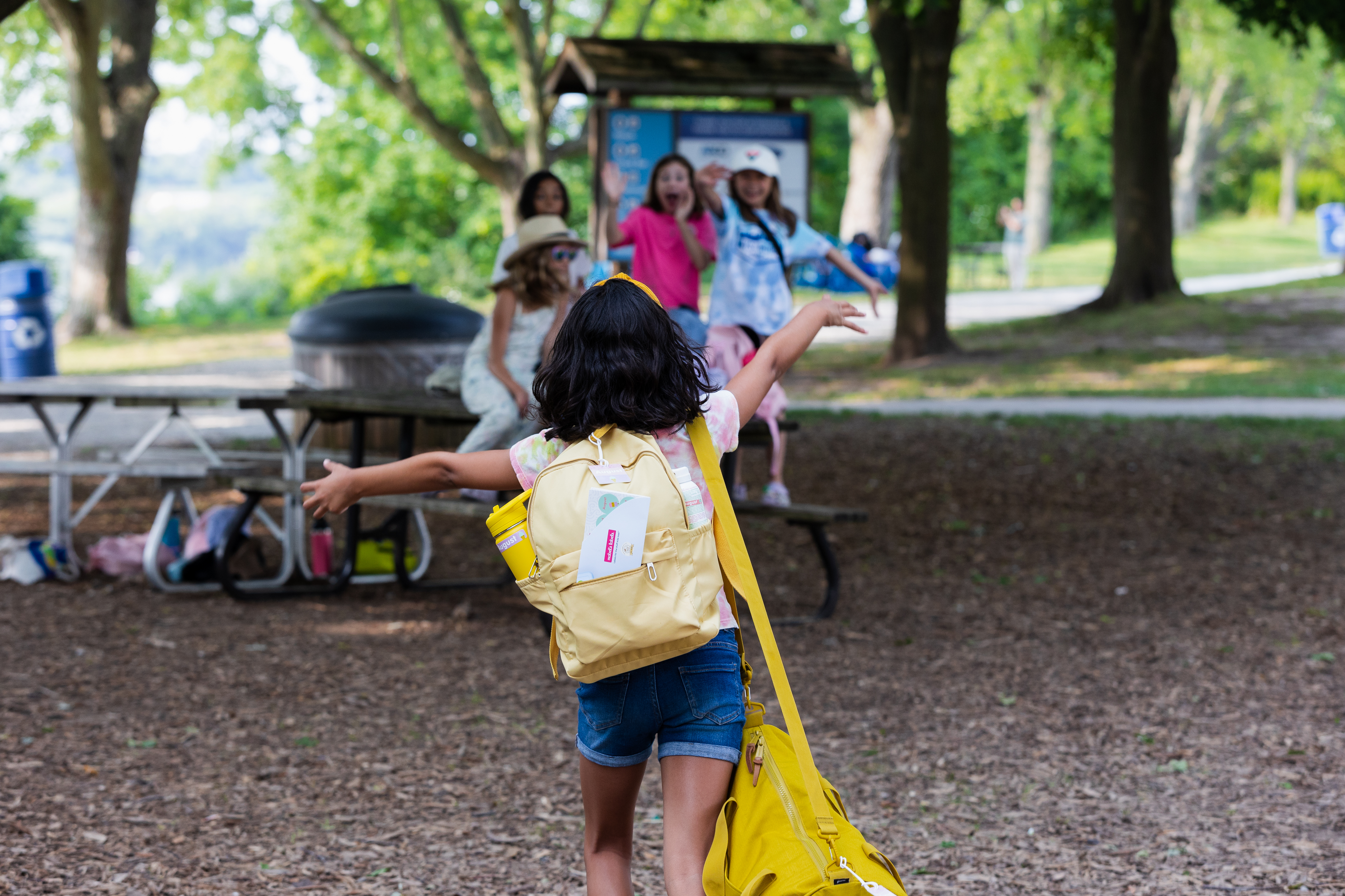 Mabel's Labels on a girl's backpack as she runs to hug her friends at camp