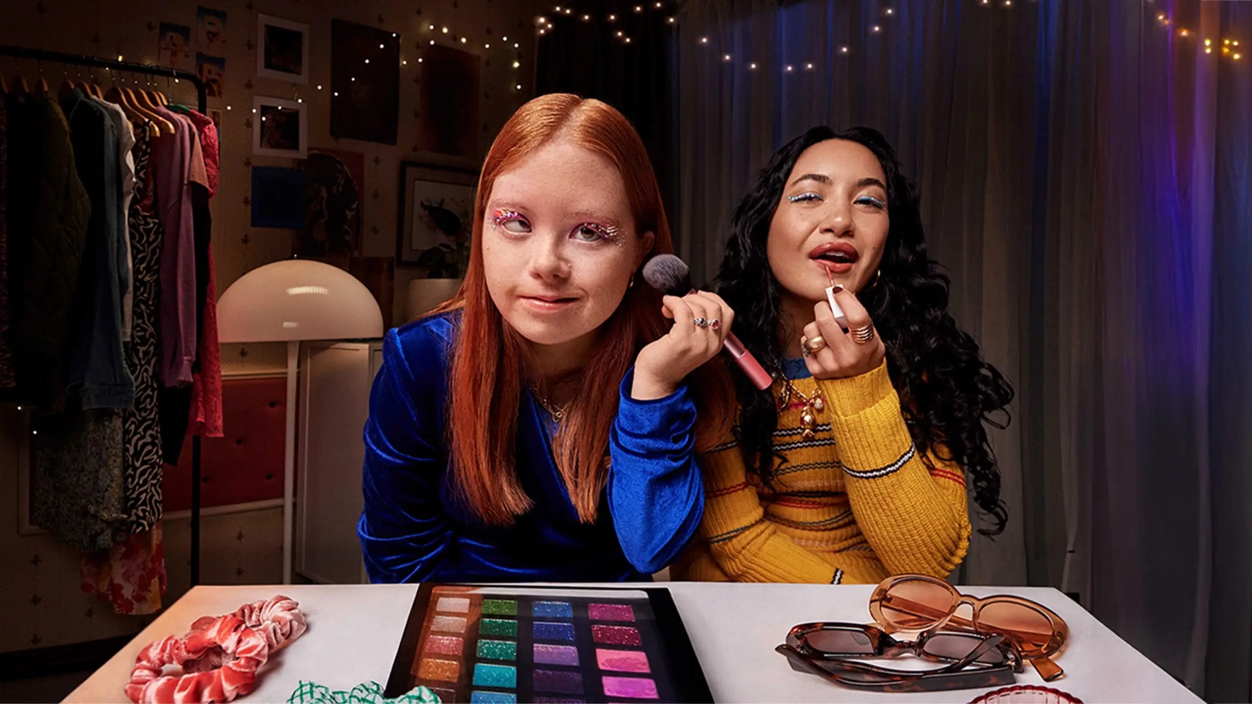 A young person and a disability support worker are looking at themselves in the mirror and smiling while applying make-up.