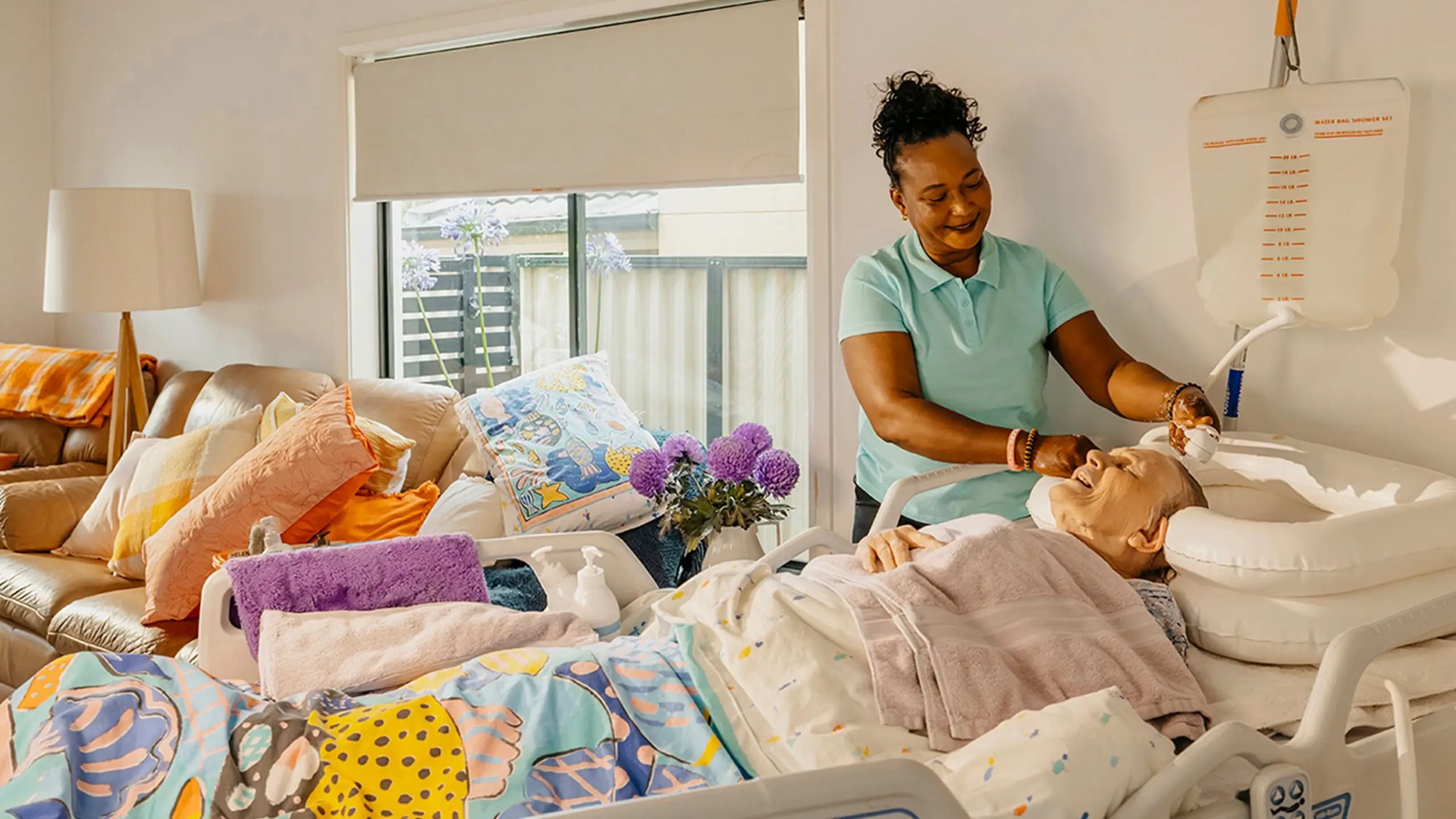Support worker washes the hair of an older person living with dementia as they lay in bed at home.
