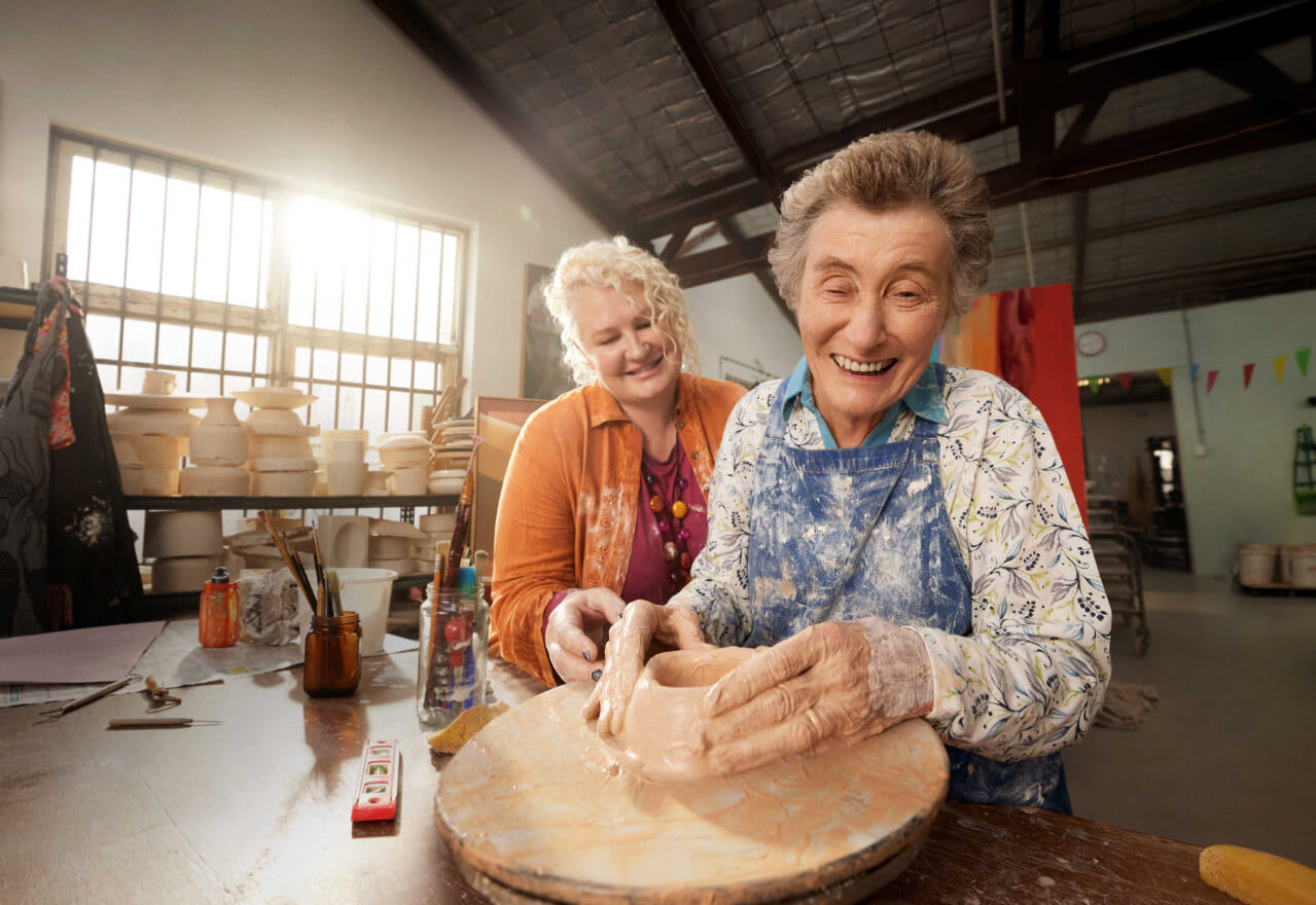 Support worker and client throwing clay on a potter's wheel together.