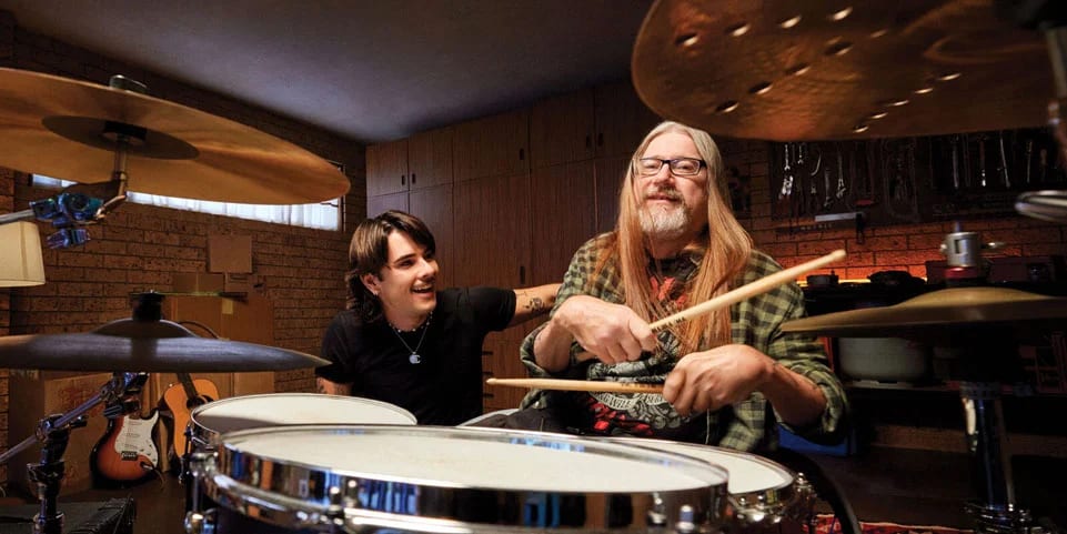 A client plays the drums while his support worker looks on.