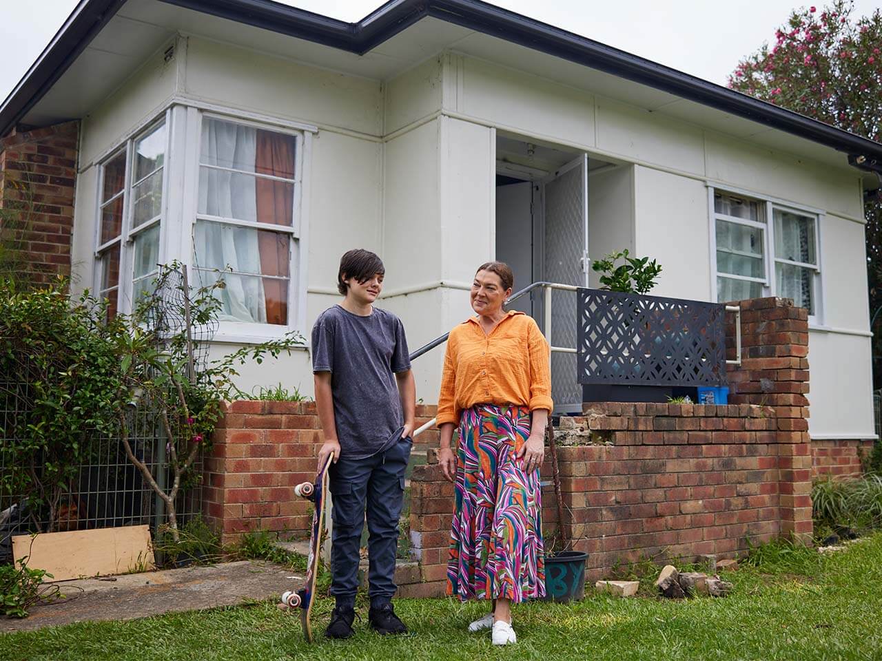 Teenager holding a skateboard standing in front of a house with support worker.