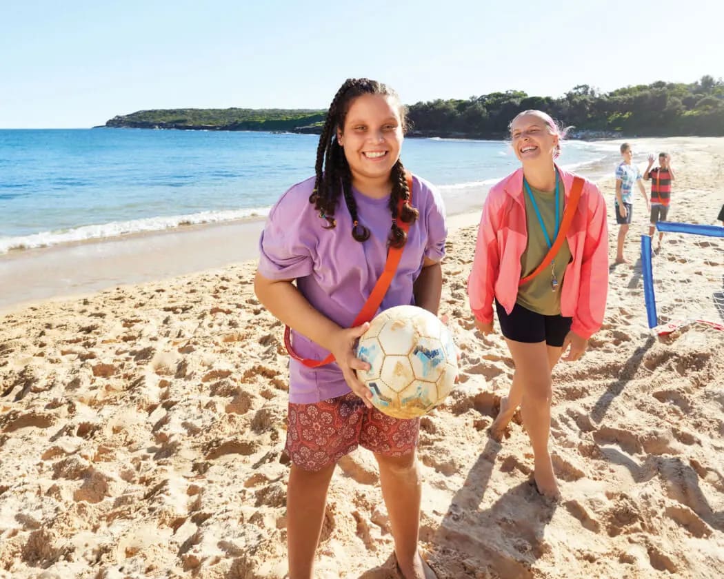 A client and her support worker play volleyball on the beach together.