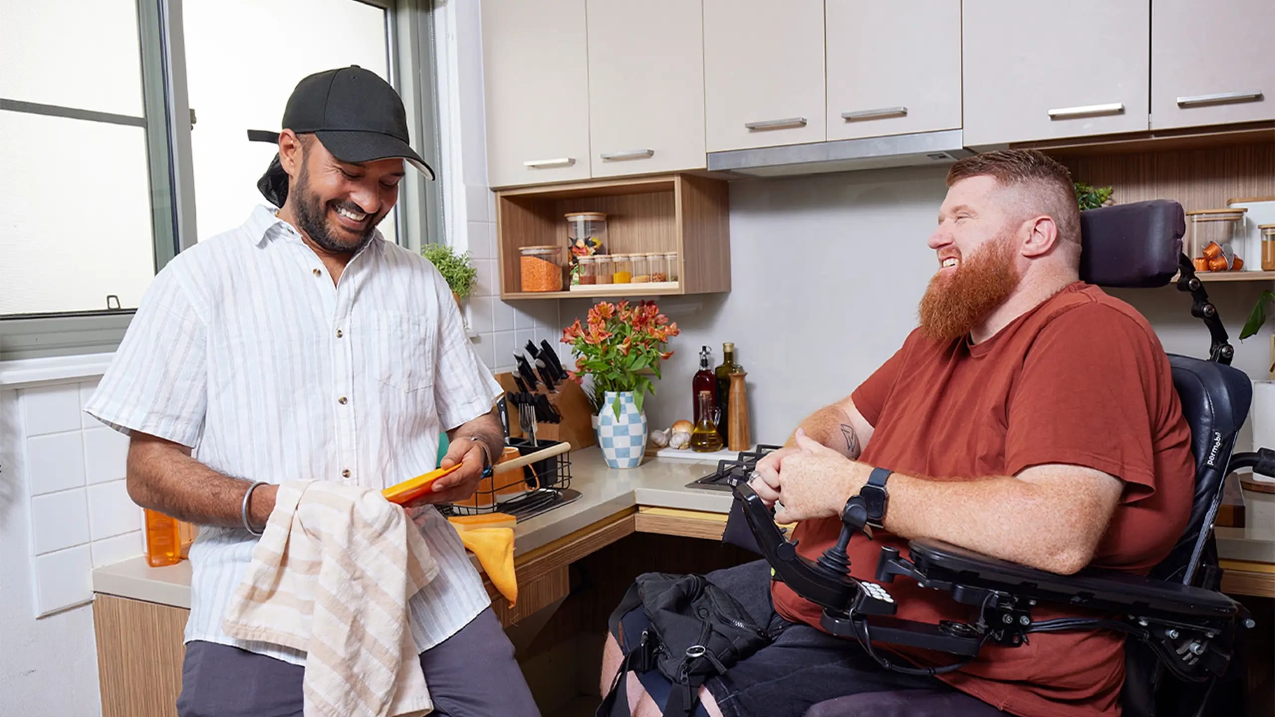 Support worker dries dishes while talking to a client who is quadriplegic and in a wheelchair.