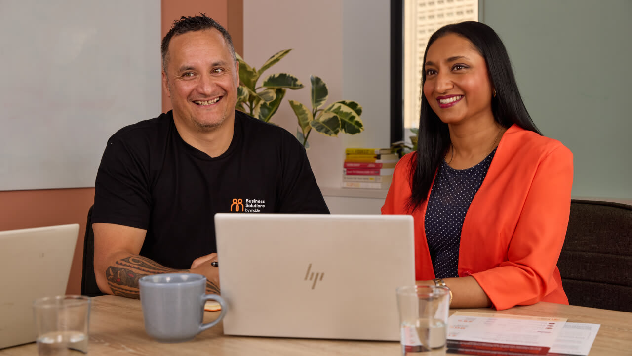 Two diverse colleagues smiling while working together at a desk with a laptop
