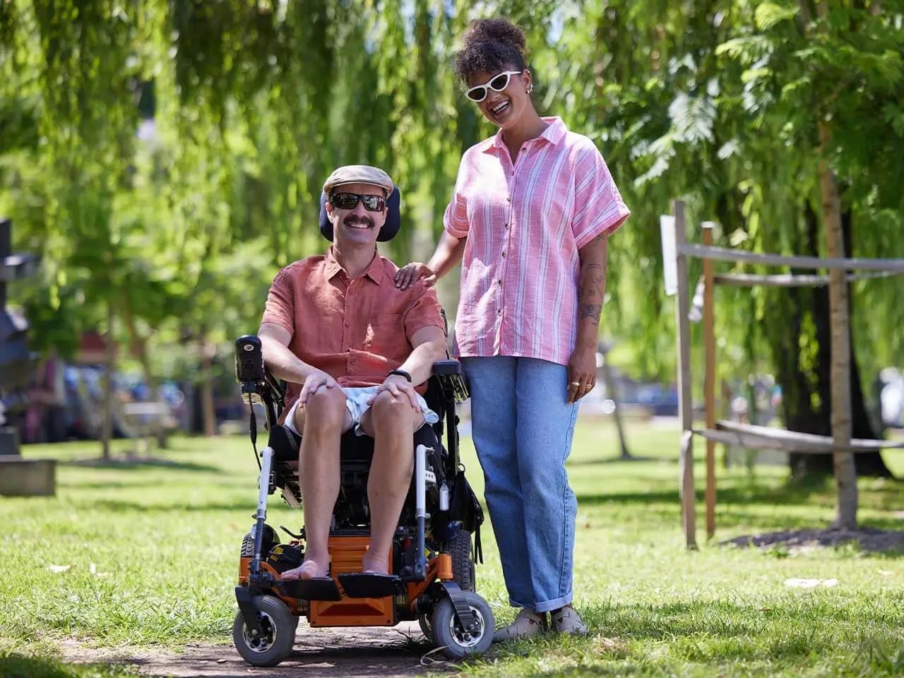 Support worker standing in a park next to client in a wheelchair.