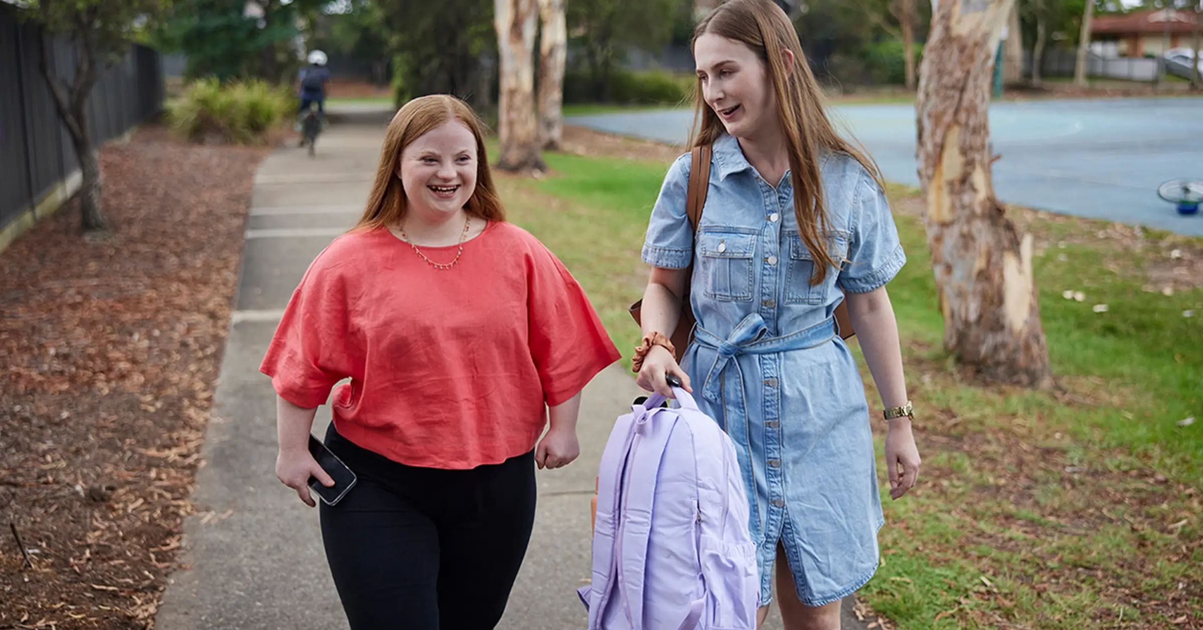 Teenager with Down syndrome walking next to support worker, who is holding a backpack.