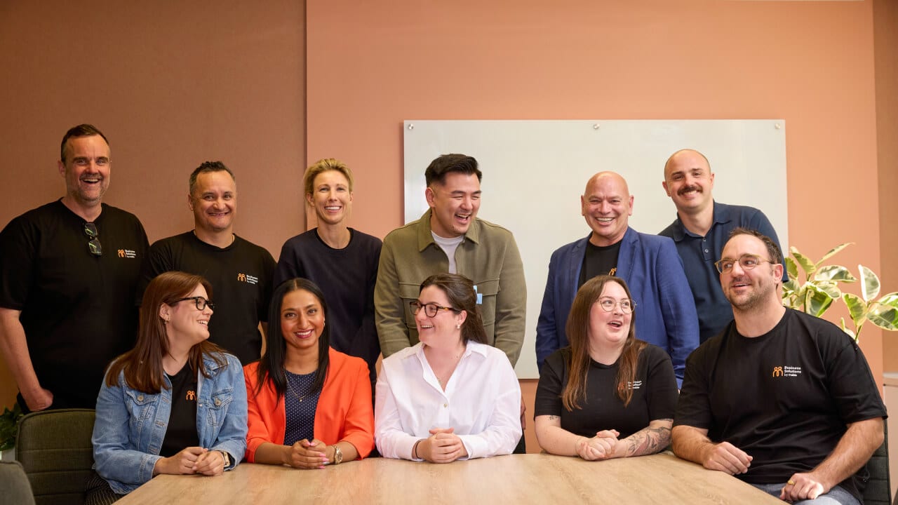 A large, diverse team of ten smiling business colleagues posing for a group photo around a conference table in an office.
