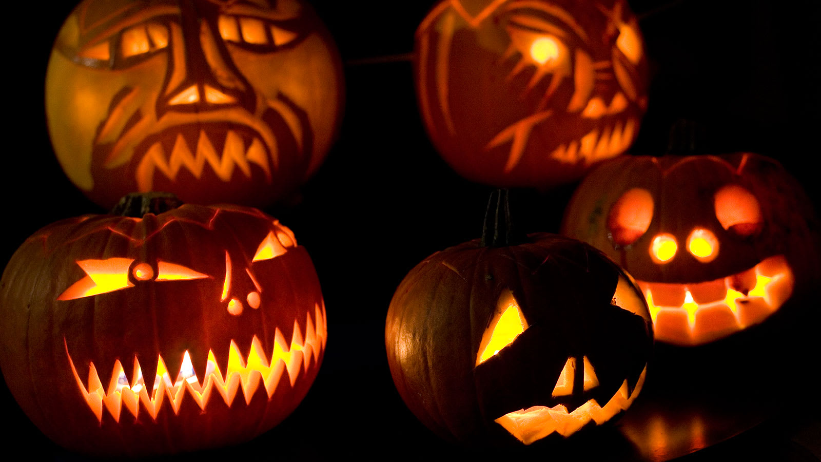 A collection of lit jackolanterns with a dark background.