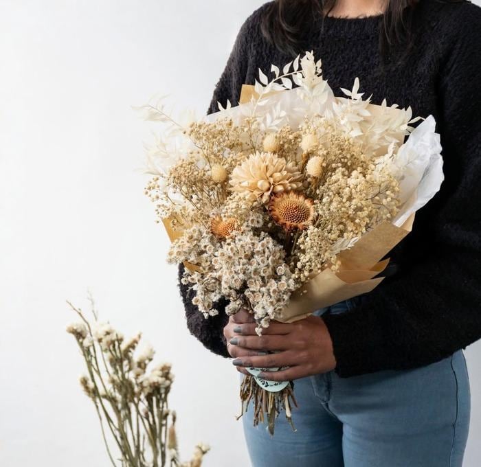 Person in a black sweater holding a large neutral-toned dried flower bouquet with golden thistles and baby's breath
