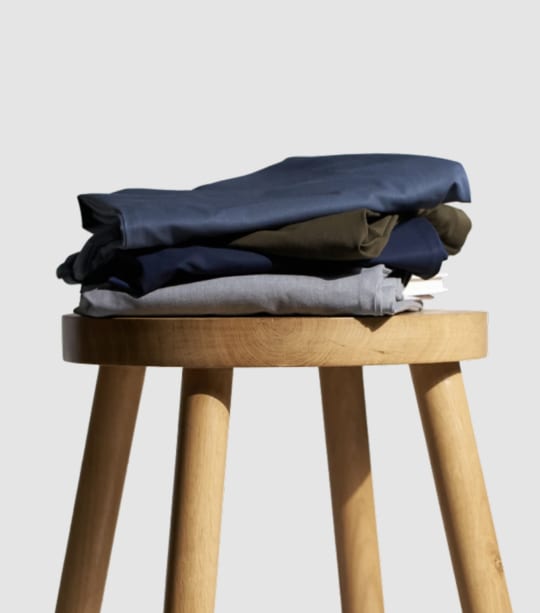 Stack of The Pant Project pants on wooden stool