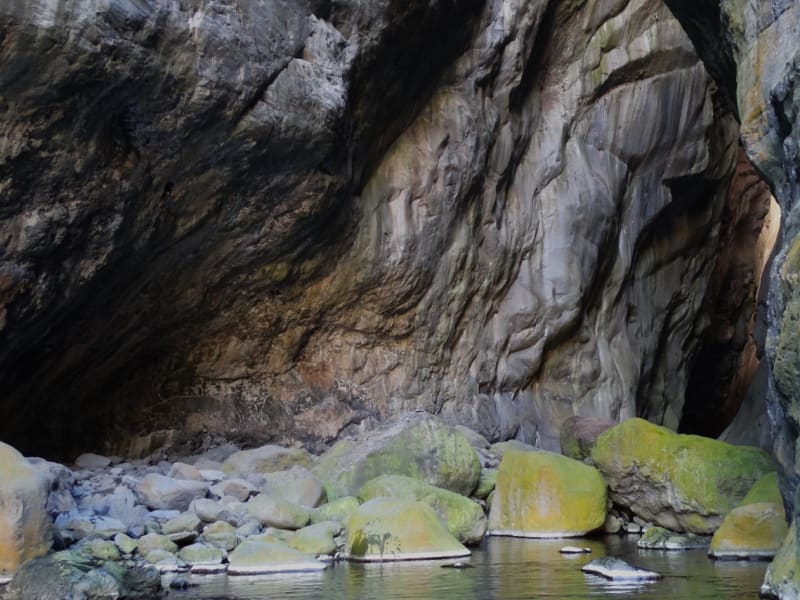 Intérieur de La Chapelle : hautes parois de roche grise sculptées par l'eau, blocs couverts de mousse au bord d'un bassin