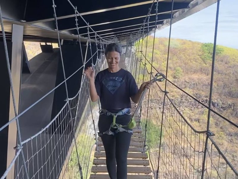 Participante souriante en harnais sur le pont de singe suspendu sous le viaduc de la ravine Fontaine, filets et câbles de part et d'autre