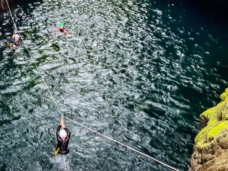 Vue plongeante sur une tyrolienne au-dessus d'un bassin sombre, un participant suspendu au câble dans la rivière Langevin