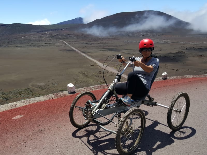 Pilote au casque rouge sur un quadbike, sur la route rouge bordée de bornes blanches, plaine de sable volcanique et reliefs en arrière-plan