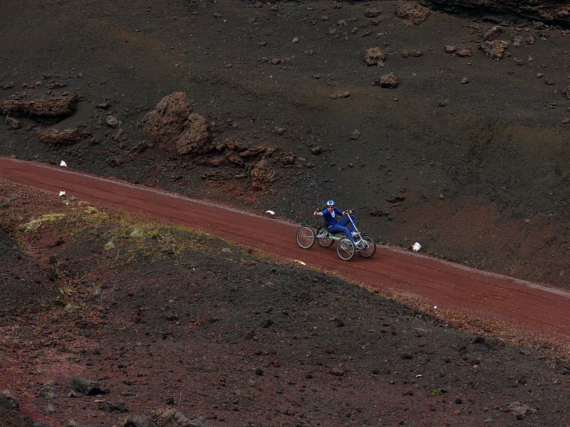 Pilote en tenue bleue sur un quadbike, seul sur une piste rouge qui coupe une pente de scories sombres