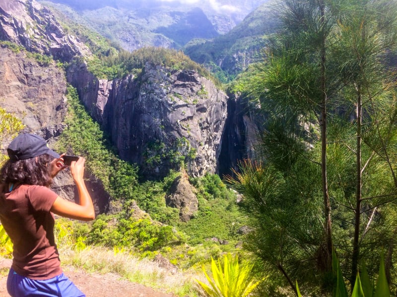 Une randonneuse photographie une gorge aux parois rocheuses verticales, entre des filaos