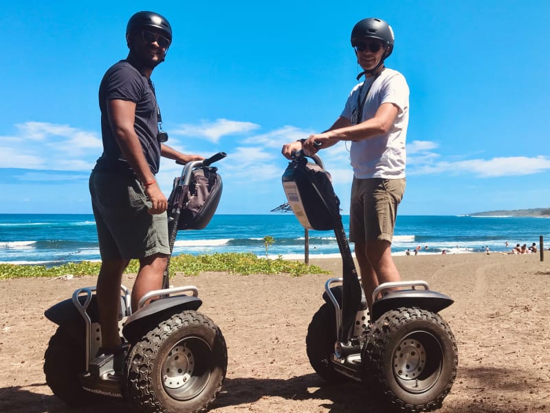 Deux pilotes casqués sur des segways tout-terrain à gros pneus sur une plage, océan et vagues en arrière-plan