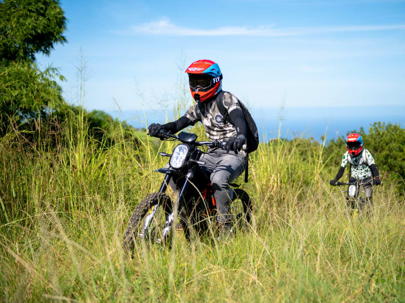 Pilote en moto électrique tout-terrain sur sentier herbeux face à l'océan Indien, casque intégral, hauteurs de Saint-Paul, La Réunion