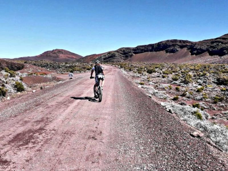 VTTAE sur piste rouge volcanique du Piton de la Fournaise, paysage minéral lunaire avec sommets en arrière-plan, La Réunion