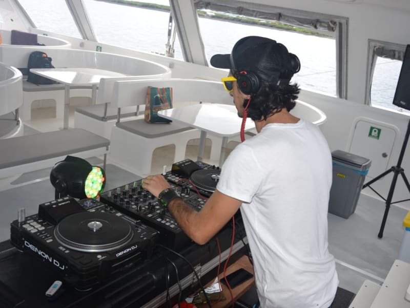DJ aux platines dans le salon intérieur d'un catamaran, enceinte sur pied et baies vitrées donnant sur la mer
