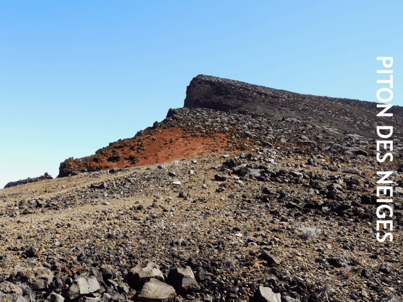 Sentier rocailleux conduisant au sommet du Piton des Neiges, croupe minérale rouge et grise du cône terminal, ciel bleu, La Réunion