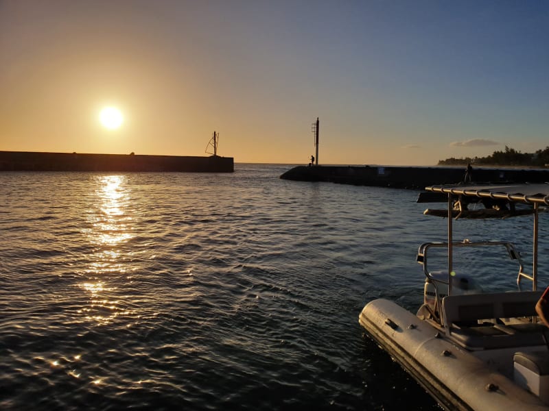 Soleil couchant entre les deux jetées de l'entrée du port de Saint-Gilles-les-Bains, un bateau semi-rigide amarré au premier plan