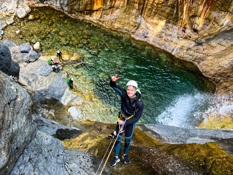 Canyoneur souriant en bas d'un rappel dans le canyon de Bras Rouge à Cilaos, parois orange suintant d'oxyde de fer, eau verte, La Réunion