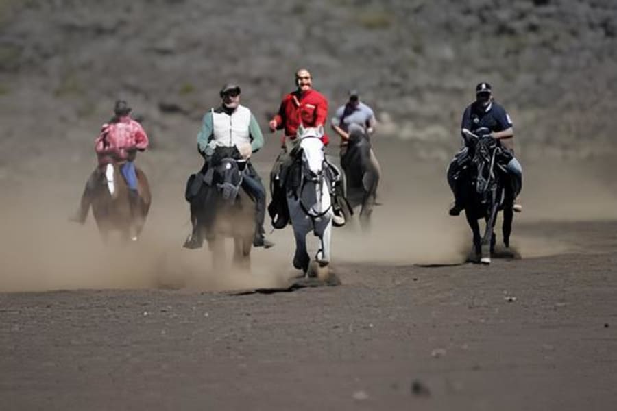 Cinq cavaliers au galop de front sur un sol de sable sombre, soulevant un nuage de poussière