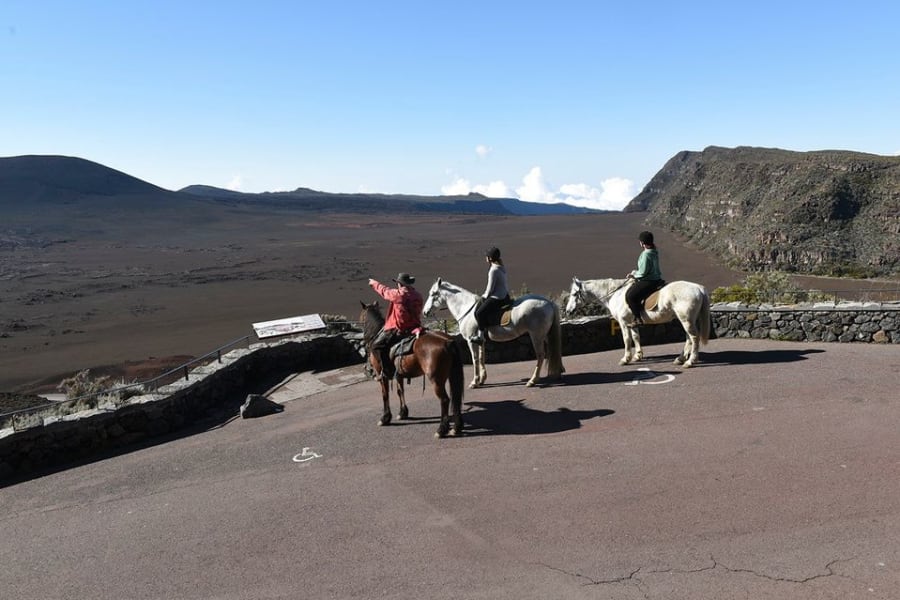 Trois cavaliers sur un belvédère bordé d'un muret de pierre, au-dessus de la Plaine des Sables, rempart sombre à droite
