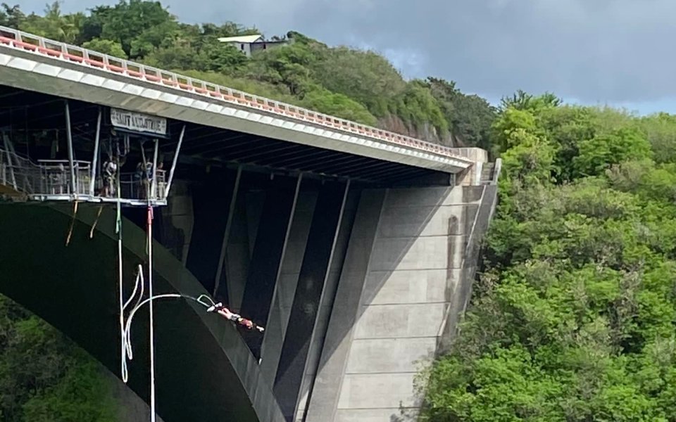 Sauteur au bout de l'élastique sous l'arche du viaduc de la ravine Fontaine, plateforme accrochée sous le tablier, végétation dense autour