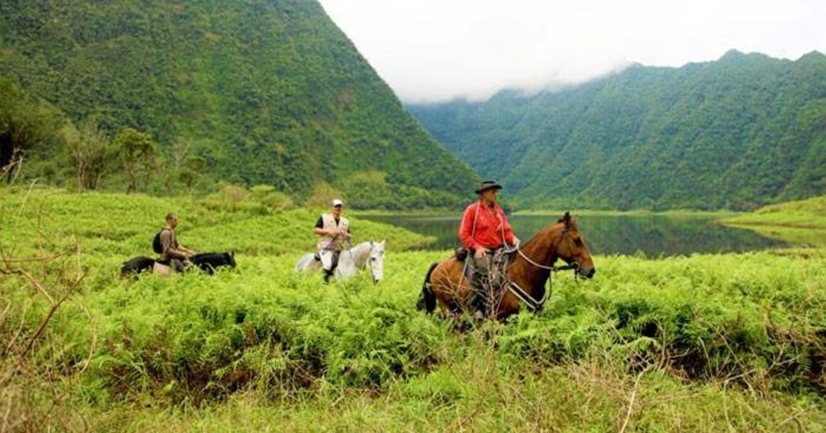 Three riders crossing the ferns beside Grand-Étang in Saint-Benoît, Reunion Island, misty mountains in the background
