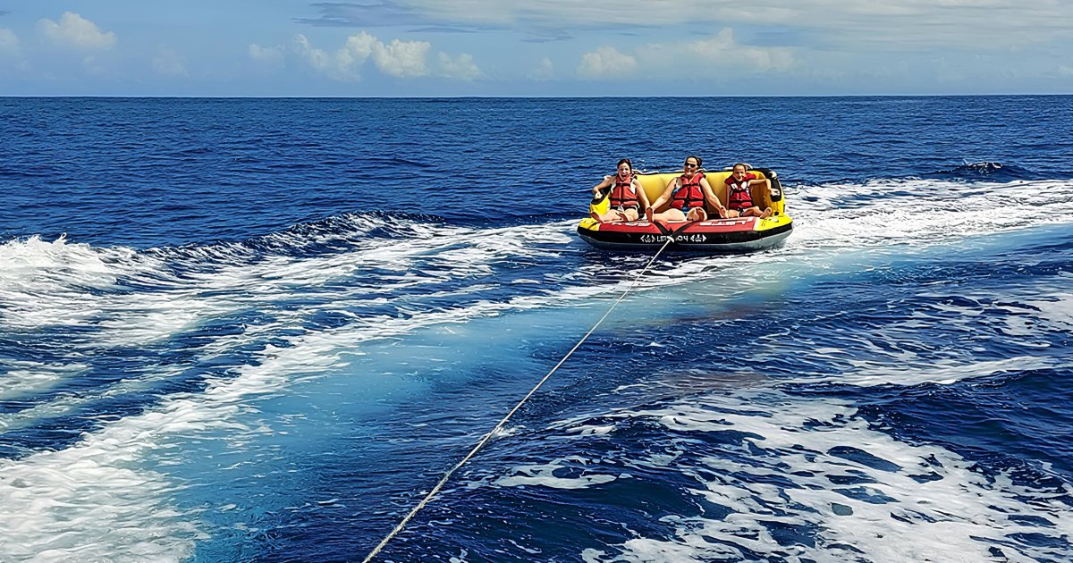 A yellow and red towable tube with 3 passengers pulled by a boat off Saint-Gilles, Reunion Island