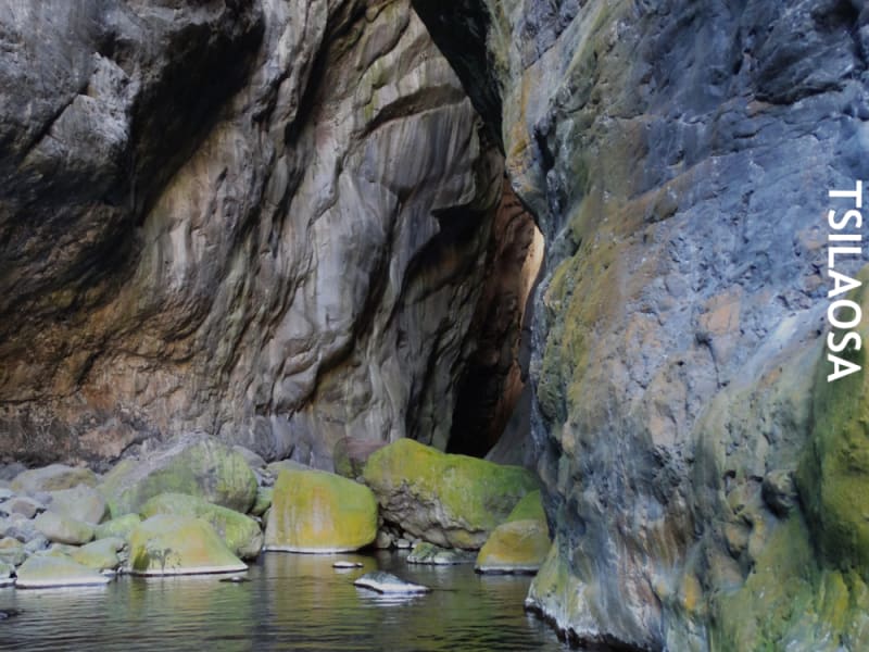 Intérieur de La Chapelle : hautes parois de roche grise sculptées par l'eau, blocs couverts de mousse au bord d'un bassin