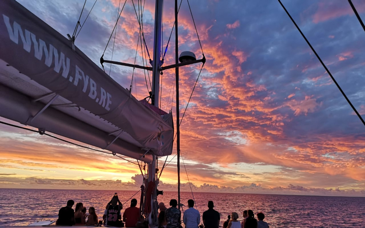 Coucher de soleil sur le pont d'un catamaran à La Réunion, ciel rose-orange et passagers admirant l'océan