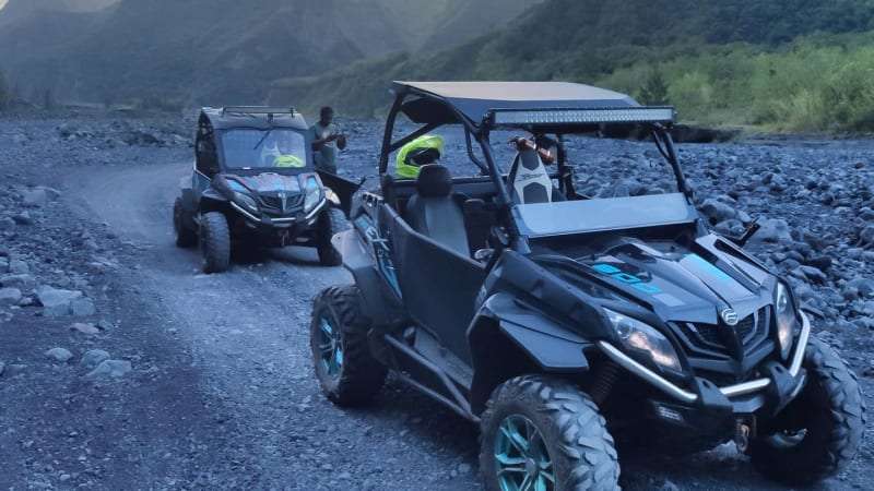 Buggy CFMOTO noir sur une piste de galets au fond d'une vallée encaissée, un second buggy derrière