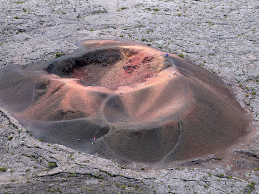 Cône du Formica Léo vu d'en haut, cratère aux teintes rouges et brunes posé sur une coulée de lave grise, quelques marcheurs sur ses flancs