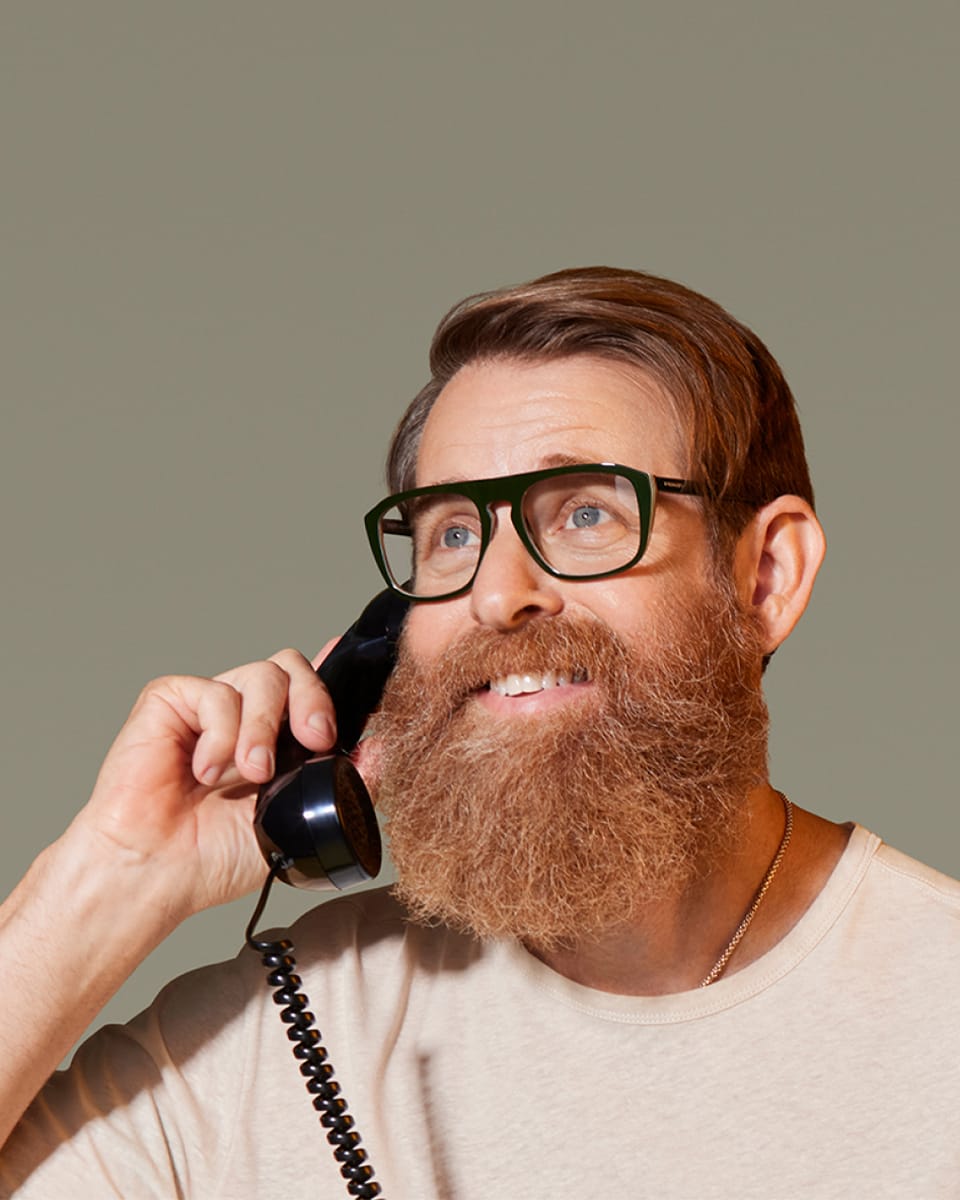 White male model wearing glasses holding an old style telephone up to his ear