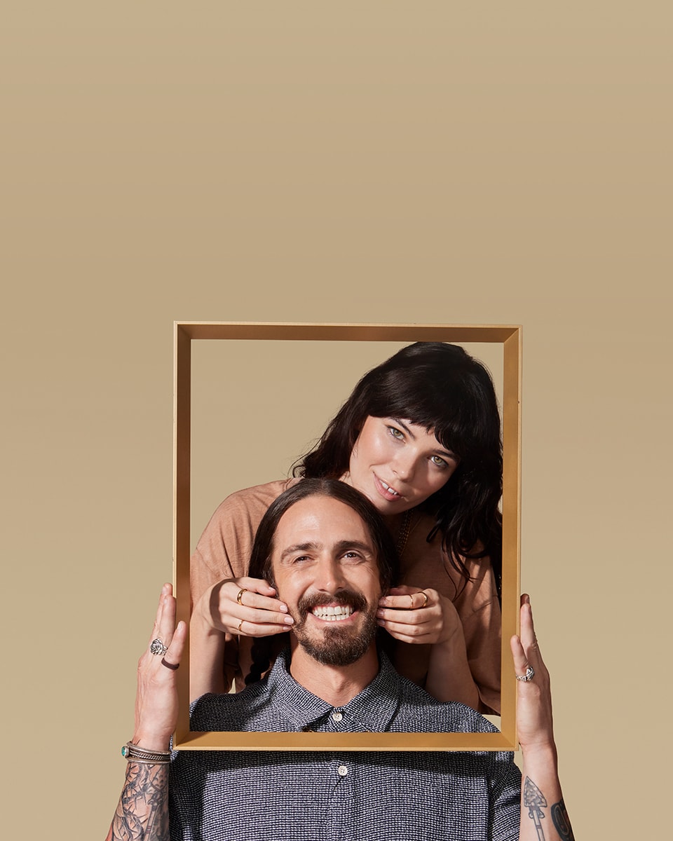 Male model sitting down smiling while having his beard rubbed by female model