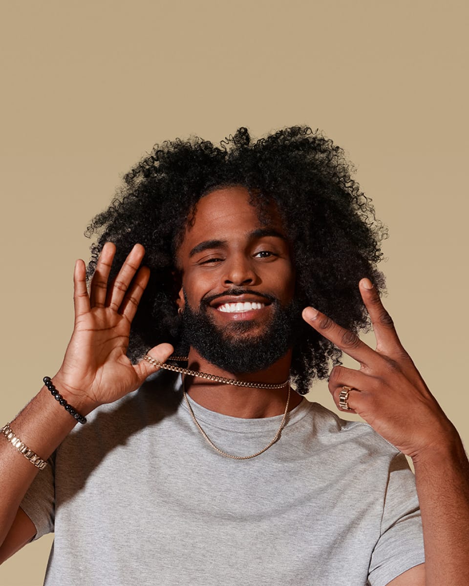 Black male model posing with a peace sign and holding his necklace